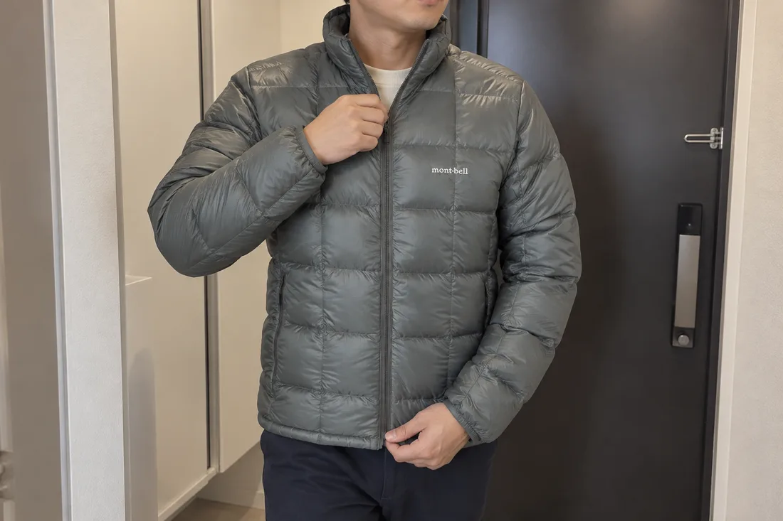 현관에서 회색 몽벨 수페리어 다운 자켓의 지퍼를 올리며 외출을 준비하는 장면